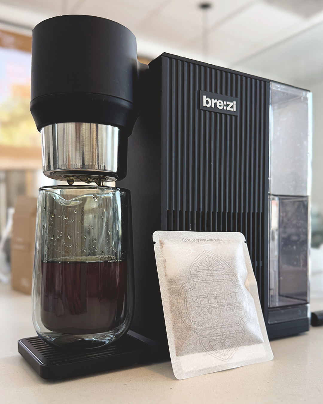 Coffee brewing device with a glass carafe and a coffee pouch, featuring the brand 'brezi'.