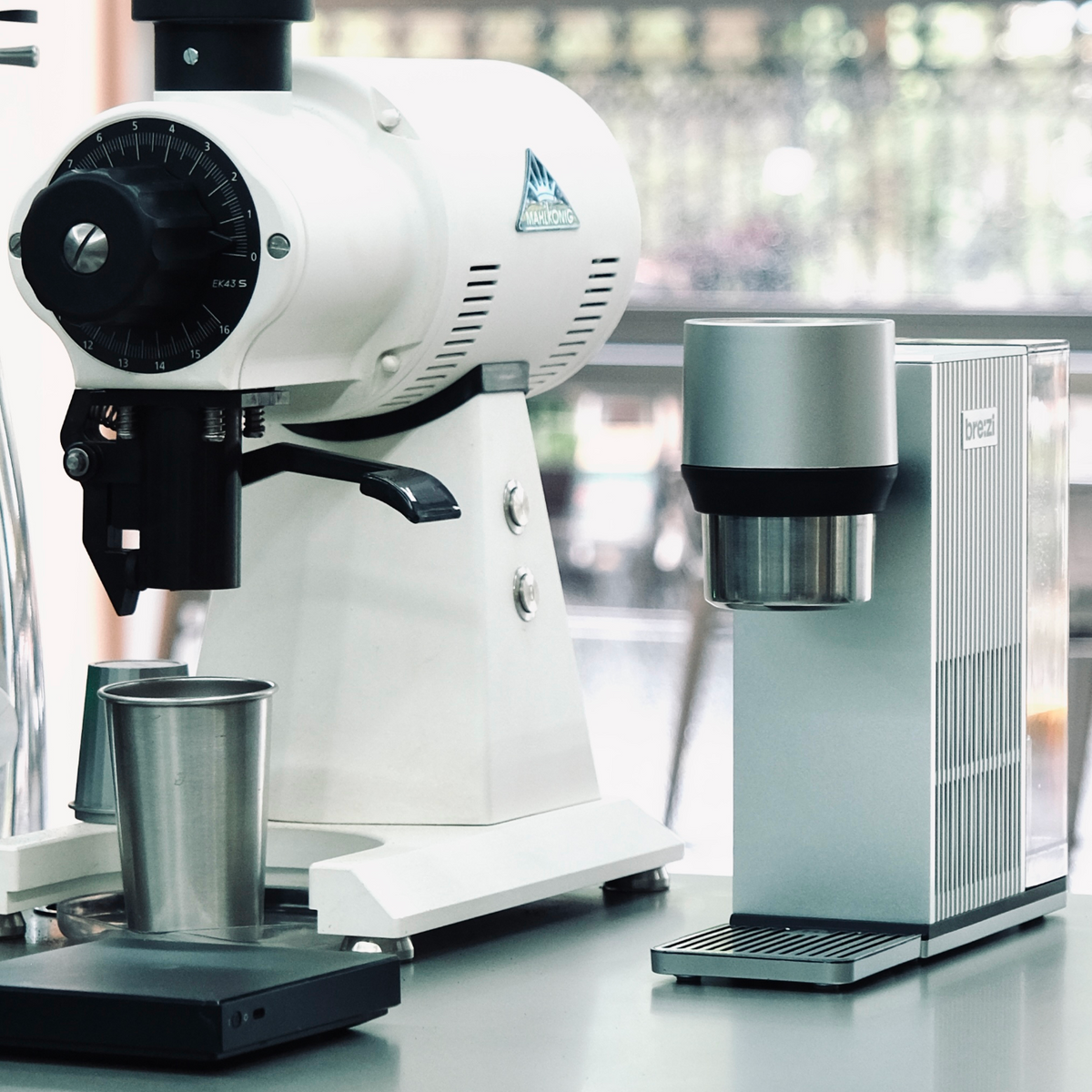 White coffee grinder and silver coffee machine on a light surface with a blurred background