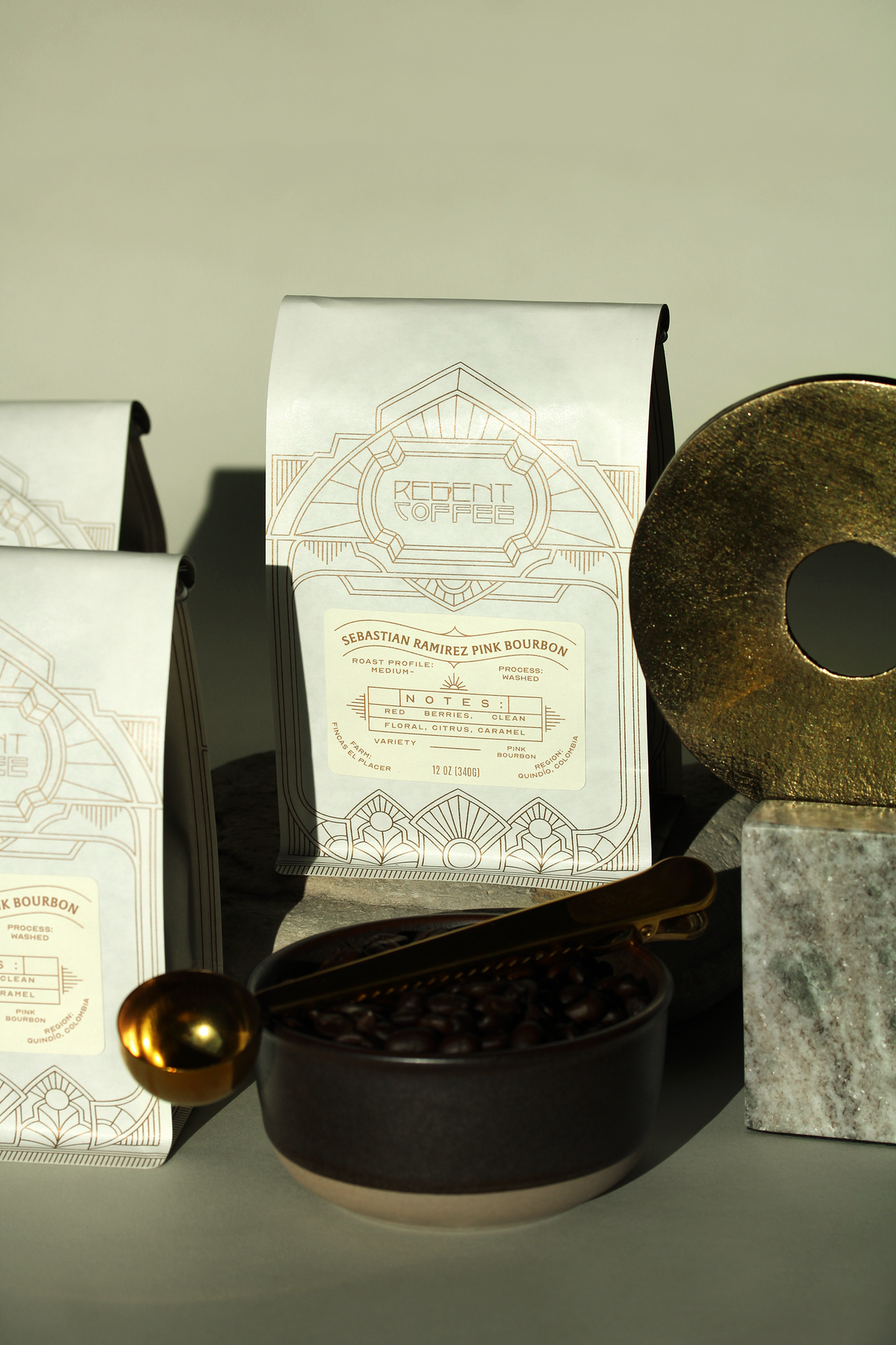 Sebastian Ramirez Pink Bourbon 12oz bag of coffee nested between another bag of coffee and a gold disc