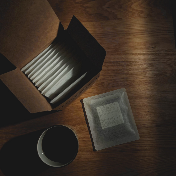 Dark wooden surface with an open box containing gray items, a small black cup, and a square gray object.